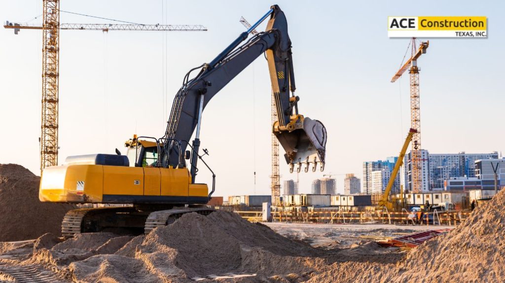A yellow excavator operates on a construction site surrounded by cranes and urban buildings, with piles of sand in the foreground.