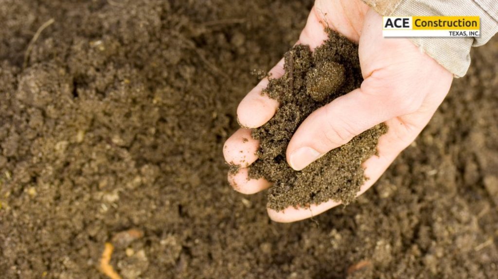 A hand holding a handful of rich brown soil against a backdrop of loose dirt, highlighting the texture and color.