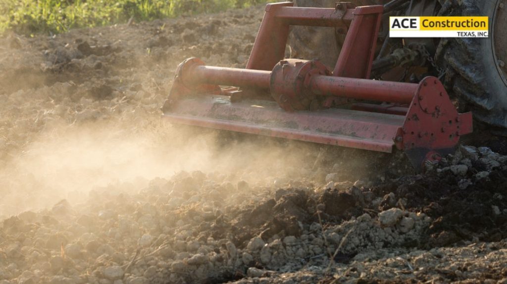 A close-up of a red tiller working on soil, creating dust as it breaks ground on a farm field, highlighting agricultural activity.