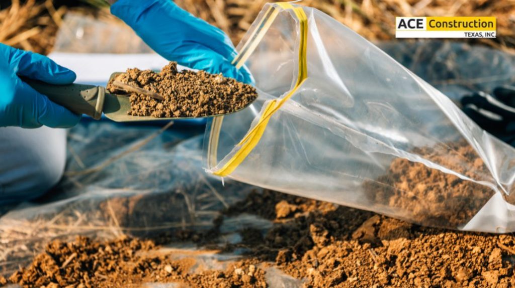 A gloved hand holding a trowel scoops soil into a clear bag on a grassy surface, indicating a construction or testing process.